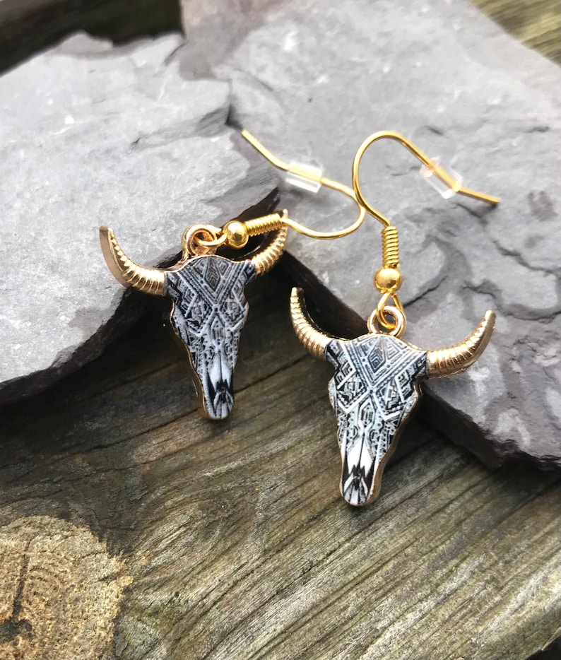 May include: A pair of gold tone earrings with a black and white patterned bull skull design.
