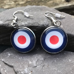 May include: A pair of silver earrings with a blue, white, and red target design. The earrings are hanging from silver hooks.
