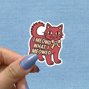 May include: A sticker with a cartoon cat in red hues and a cream bow tie. The text "I MEOWD WHAT I MEOWED" is displayed on the cat's body. The sticker is set against a light blue textured background.