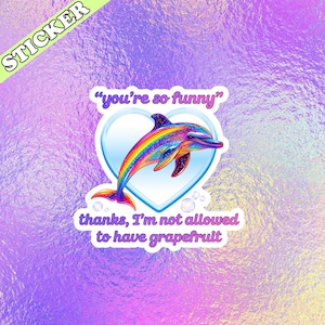Peut inclure: Autocollant avec un dauphin aux couleurs de l'arc-en-ciel dans un c&oelig;ur, avec le texte "you're so funny" et "thanks, I'm not allowed to have grapefruit". Le mot "STICKER" est en haut &agrave; gauche. Fond iris&eacute;.