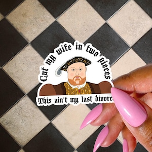 May include: A sticker featuring a cartoon illustration of King Henry VIII with the text "Cut my wife in two pieces" and "This ain't my last divorce." The sticker is held by a hand with pink nails.