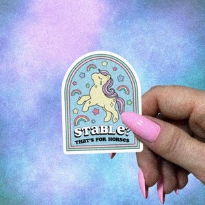 May include: A sticker with a light yellow unicorn design, a rainbow, and the text "Stable? That's for Horses." The sticker has a light blue background with stars and rainbows.