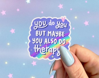 Puede incluir: Una pegatina con el texto "you do you BUT MAYBE YOU ALSO DO therapy" en forma de nube morada con un arcoíris y estrellas. El fondo es azul claro con estrellas rosas.