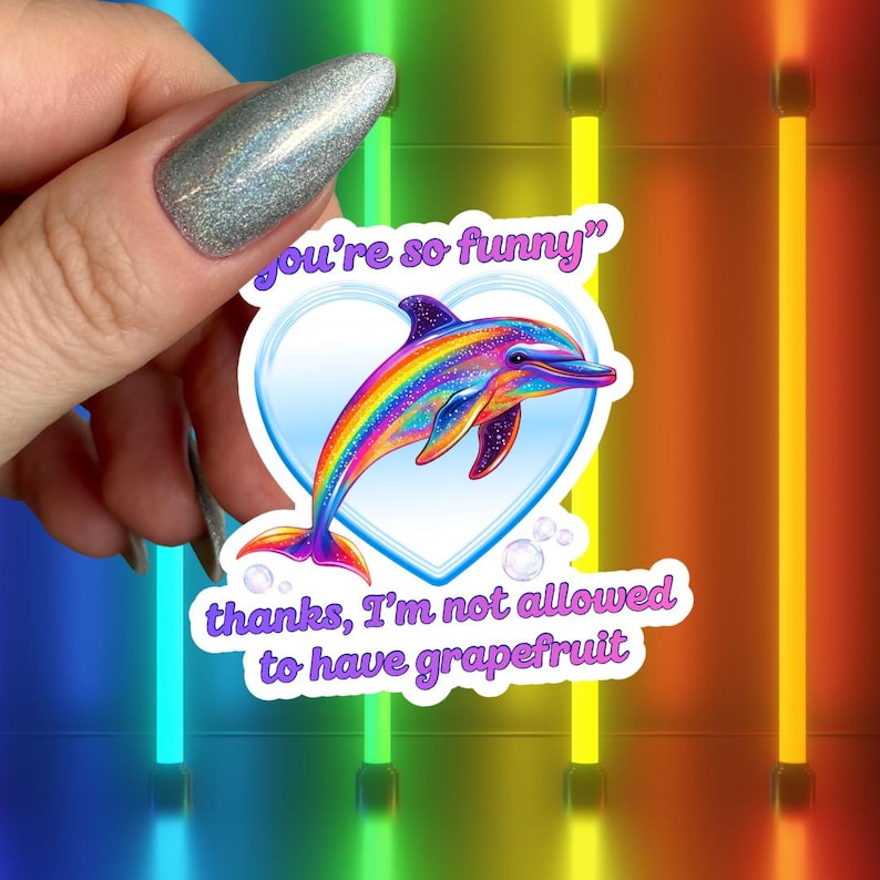 Peut inclure: Un autocollant de dauphin color&eacute; avec un design arc-en-ciel, encadr&eacute; dans un c&oelig;ur. Le texte sur l'autocollant dit "you're so funny" et "thanks, I'm not allowed to have grapefruit".