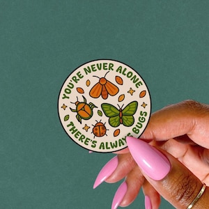 May include: A circular sticker with a cream background. It features cartoon insects and the text "YOU'RE NEVER ALONE THERE'S ALWAYS BUGS". The sticker has a green beetle, orange moth, green butterfly, and red ladybug.