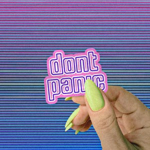 May include: A sticker with the words "dont panic" in a pink and white outlined font. The sticker is held by a hand with long, light green nails against a background of blue and pink horizontal lines.