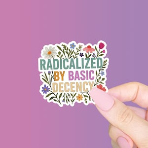 May include: A sticker with the text "RADICALIZED BY BASIC DECENCY" in a colorful, floral design. The sticker features a variety of flowers in shades of pink, blue, yellow, and white, with green leaves. The background is a gradient of purple and pink.