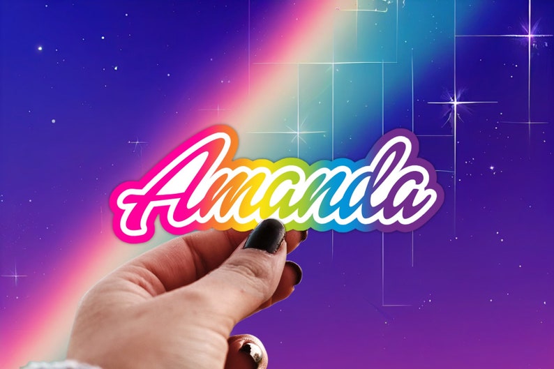 May include: A rainbow-colored sticker with the name "Amanda" written in white letters. The sticker is being held by a hand against a purple and blue background with white stars.