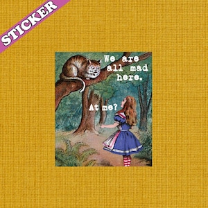 May include: A sticker featuring an illustration from Alice in Wonderland. The image shows the Cheshire Cat on a tree branch, with Alice below. Text reads "We are all mad here" and "At me?" The sticker has a yellow background.