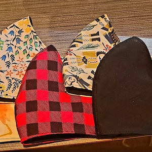 May include: Five fabric face masks, each with a different pattern. The masks are arranged in a row, with the black mask at the front. The patterns include a leopard print, a floral print, a plaid print, and a geometric print.