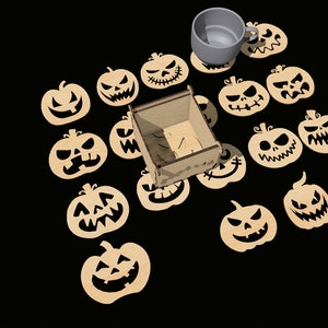 May include: A set of 15 wooden pumpkin-shaped coasters with black jack-o'-lantern faces. The coasters are arranged around a small wooden box and a gray ceramic mug.