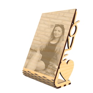 Op de afbeelding: Een houten fotolijst met een hartvormige basis en het woord "LOVE" in de zijkant gegraveerd. De lijst bevat een foto van een persoon met een zonnebril.
