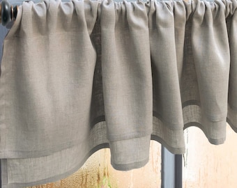 May include: A light gray linen valance with a ruffled edge hangs over a window with condensation on the glass.