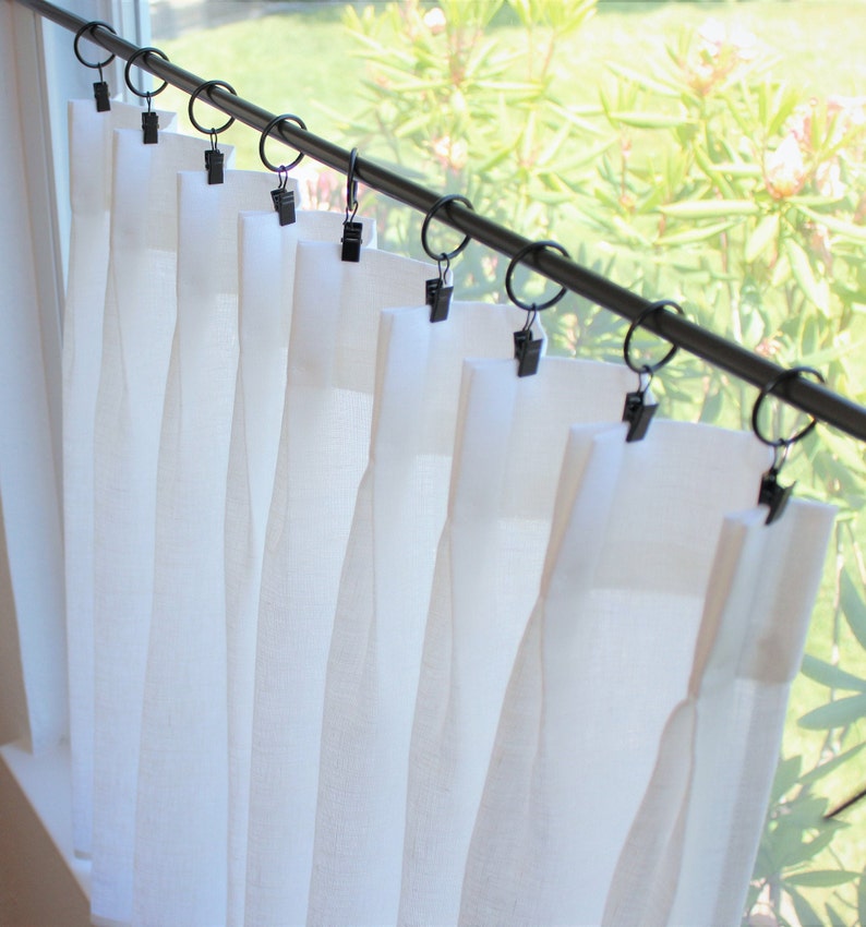 May include: White sheer curtains with pleats hanging from a black curtain rod with black clips.