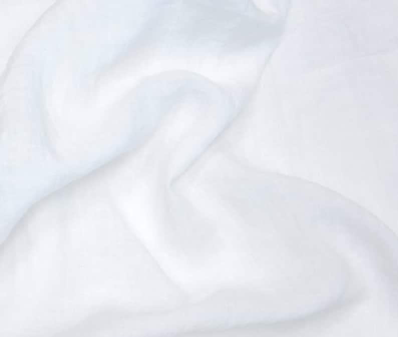 May include: White fabric with a soft, smooth texture. The fabric is wrinkled and folded, creating a natural, organic look.