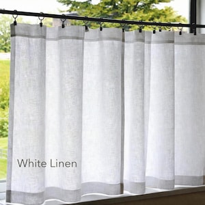 May include: A white linen curtain panel featuring a semi-sheer, textured weave. The curtain is suspended from a black metal rod by a series of black metal rings with clips. The text White Linen is printed in a simple font on the lower left side.