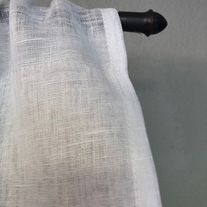 Pode incluir: Cortina branca transparente com textura de linho pendurada em uma haste de cortina de metal preto com uma ponta decorativa.