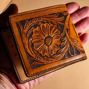 May include: A brown leather wallet with a floral design embossed on the front. The design features a large flower with intricate details.