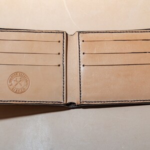 May include: A brown leather wallet with multiple card slots and a stitched border. The wallet is open and has a logo that reads "Brenton Saddlery Maker" in a circle.