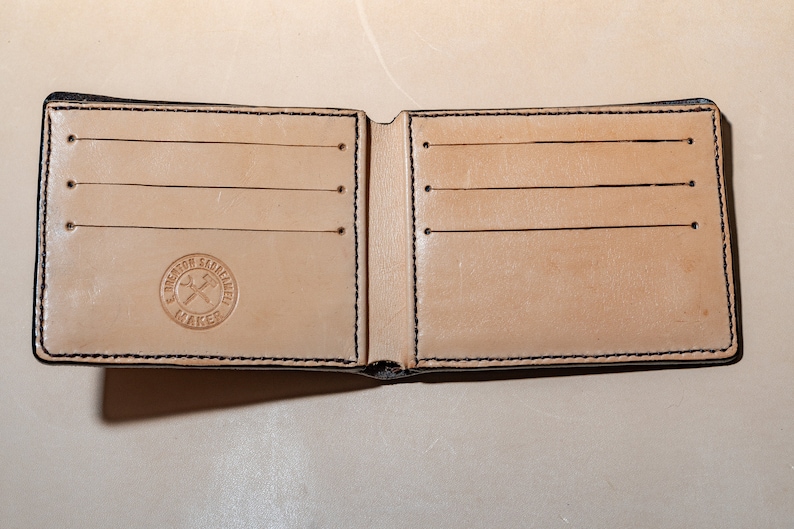 May include: A brown leather wallet with multiple card slots and a stitched border. The wallet is open and has a logo that reads "Brenton Saddlery Maker" in a circle.