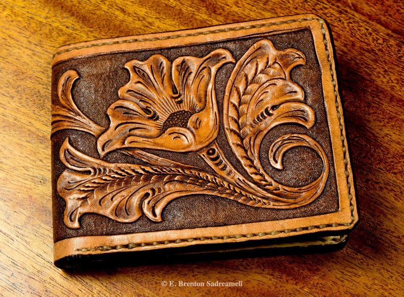 May include: A brown leather wallet with a tooled floral design. The design features a large flower with intricate details and leaves.