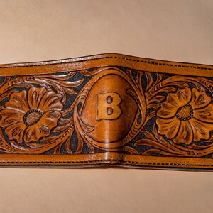May include: A brown leather wallet with a floral design and the letter "B" embossed in the center.