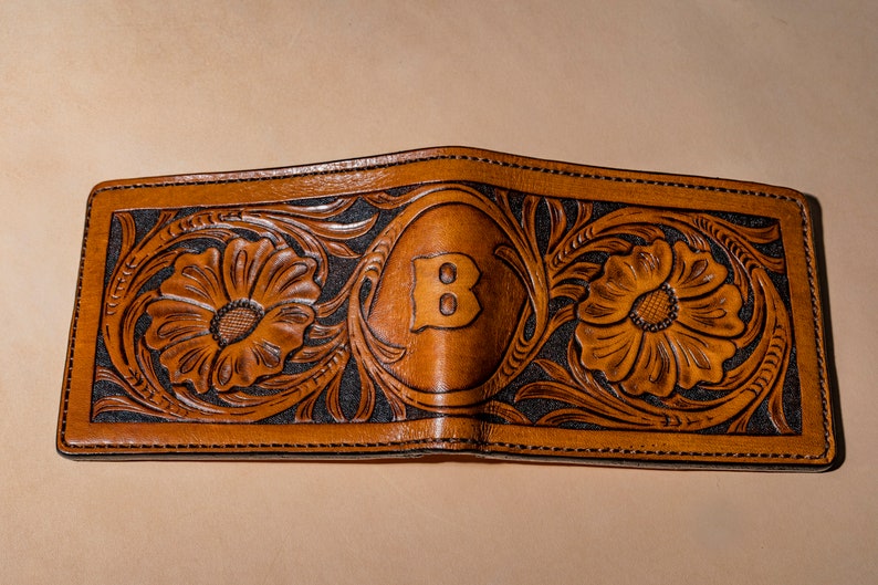 May include: A brown leather wallet with a floral design and the letter "B" embossed in the center.