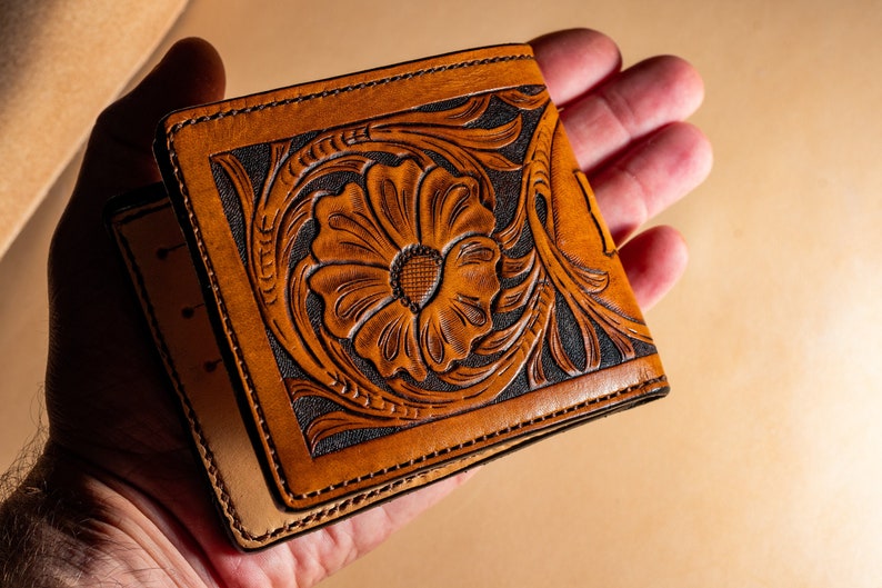 May include: A brown leather wallet with a floral design embossed on the front. The design features a large flower with intricate details.
