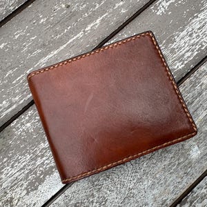 May include: A brown leather wallet with a stitched edge.