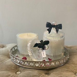 Puede incluir: Dos tarros de vela de vidrio transparente con velas blancas y lazos de cinta negra. Los tarros están en una bandeja plateada con diamantes de imitación alrededor del borde.