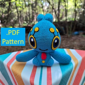 Könnte beinhalten: Ein blaues Häkel-Plüschtier mit großem Kopf, gelb umrandeten Augen, gelben Antennen und einem roten runden Fleck auf der Brust. Ein blaues Quadrat mit dem gelben Text .PDF Pattern ist links neben dem Plüschtier zu sehen.