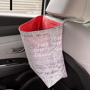 以下が含まれることがあります： ヘッドレストから吊り下げられた布製の車用ゴミ袋。ライトグレーの外側には「little things」、「our nest is blessed」、「home is who we share it with」という筆記体の文字がプリントされており、内側は鮮やかな赤色の裏地になっています。