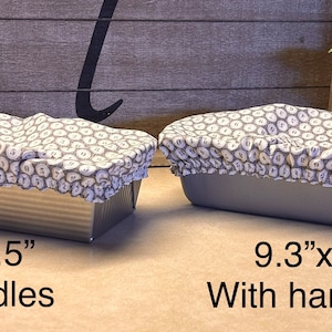 May include: Two loaf pans with grey and white patterned fabric covers. The pan on the left is 8.5 inches by 4.5 inches and does not have handles. The pan on the right is 9.3 inches by 5 inches and has handles.
