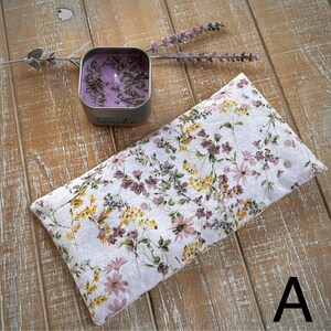 Op de afbeelding: Een rechthoekig kussen met een bloemenpatroon in wit, paars, geel en groen. Daarnaast een kleine, vierkante zilveren kaarsenpot met een paarse kaars en lavendelknopjes. Op de pot staat "Lavender".