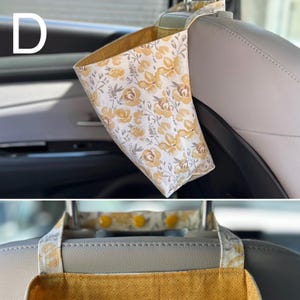 以下が含まれることがあります： 黄色とグレーの花柄が施された白い布製の車用ゴミ袋。3つの黄色いプラスチックスナップで留められたストラップを使用して、車のヘッドレストに吊り下げられています。内側の裏地は無地のマスタードイエローの布地です。
