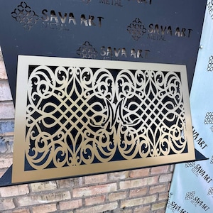 May include: A gold-coloured metal decorative panel with an intricate, symmetrical cutout design. The panel is rectangular and features swirling patterns and geometric shapes. The words "SAVA ART METAL" are visible in the background.