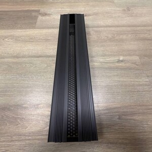 May include: A black metal vent cover with a rectangular shape and a series of vertical lines. The vent cover has a perforated metal insert with a grid pattern.