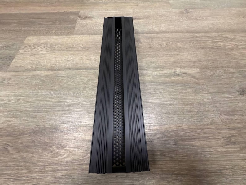 May include: A black metal vent cover with a rectangular shape and a series of vertical lines. The vent cover has a perforated metal insert with a grid pattern.