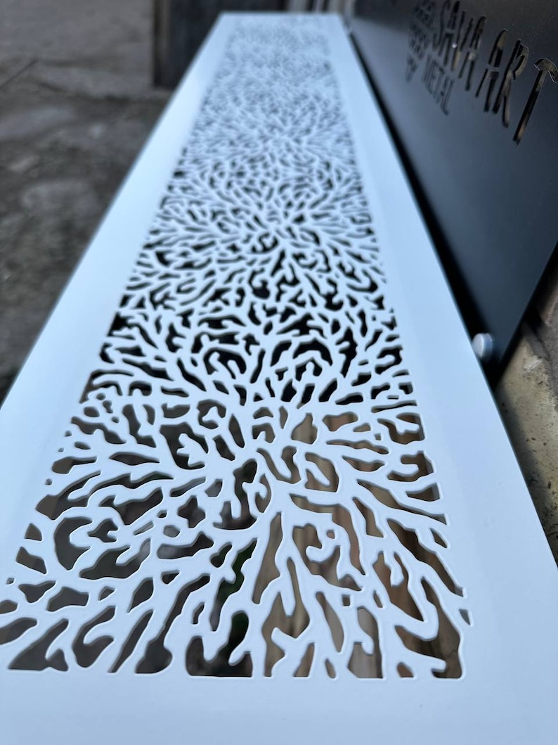 May include: White metal vent cover with a decorative, intricate, laser-cut design resembling branches or coral. The design is repeated vertically across the cover.