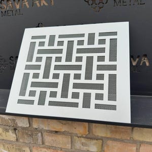 May include: White metal ventilation grille with a geometric pattern of squares and rectangles. The grille is made of metal and has a white finish.
