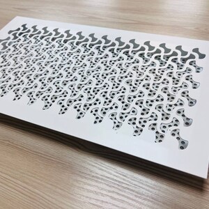 K&ouml;nnte beinhalten: Wei&szlig;er L&uuml;ftungsgitter aus Metall mit einem dekorativen Muster aus sich wiederholenden geschwungenen Formen. Das Muster ist aus dem Metall ausgeschnitten und bildet ein Gitter aus kleinen L&ouml;chern.