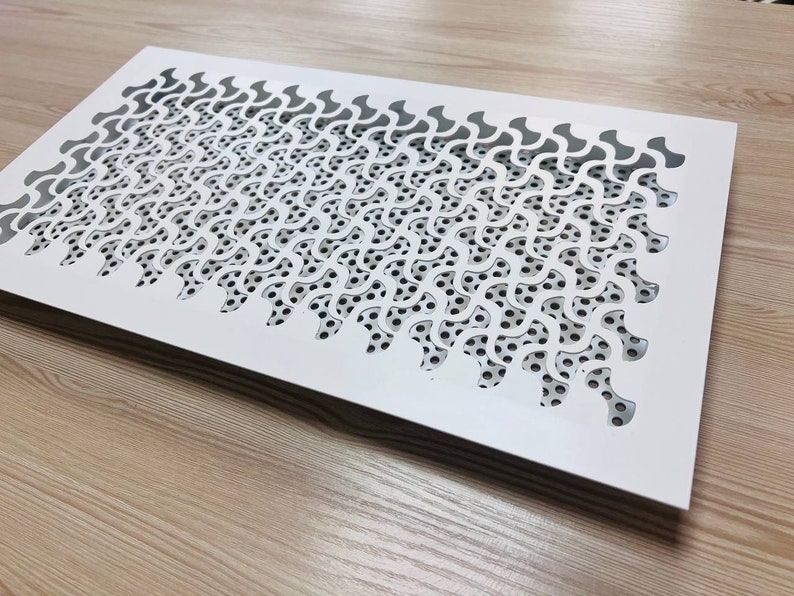 K&ouml;nnte beinhalten: Wei&szlig;er L&uuml;ftungsgitter aus Metall mit einem dekorativen Muster aus sich wiederholenden geschwungenen Formen. Das Muster ist aus dem Metall ausgeschnitten und bildet ein Gitter aus kleinen L&ouml;chern.