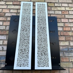 May include: Two white metal panels with a decorative, intricate, floral pattern. The panels are mounted on a black background with the word "ART" repeated three times.