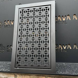 以下が含まれることがあります： 幾何学模様の黒い金属製の装飾スクリーン。スクリーンは壁に取り付けられており、金属から切り抜かれた「SAVA ART METAL」という文字があります。