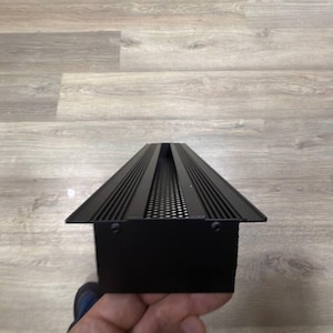 May include: Black metal vent cover with a rectangular shape and a series of horizontal lines and a small grid pattern.