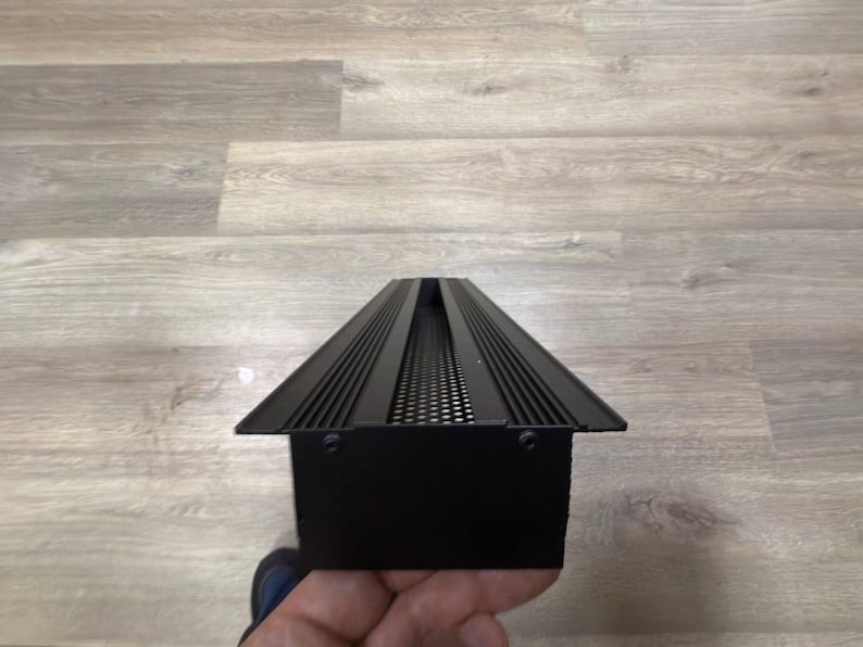 May include: Black metal vent cover with a rectangular shape and a series of horizontal lines and a small grid pattern.