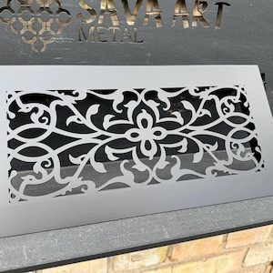 May include: A gray metal decorative panel with a floral and scrollwork design. The panel has a rectangular frame and is placed in front of a dark gray surface with the text "SAVA ART METAL".