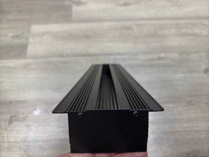 May include: Black metal light fitting with a rectangular shape and a long, narrow opening in the centre. The opening has a series of small holes along the sides.