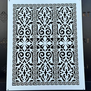 Puede incluir: Plantilla de metal blanco con un diseño intrincado negro que presenta un patrón repetitivo de motivos florales y un borde de clave griega.