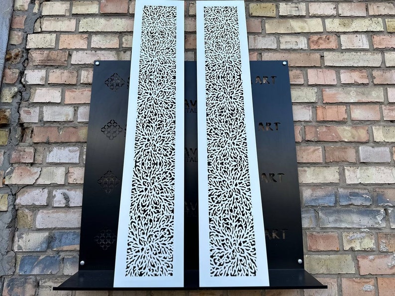 May include: Two white metal panels with a decorative, intricate, floral pattern. The panels are mounted on a black background with the word "ART" repeated vertically.